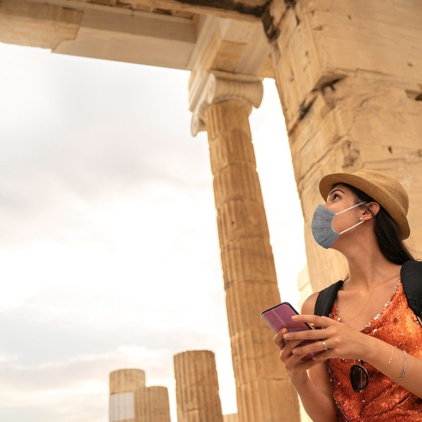 Tourist using face mask and using smartphone visiting ancient greek city